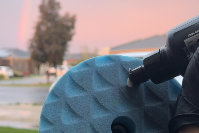 Applying compound during a paint correction service, with a rainbow backdrop highlighting the process.